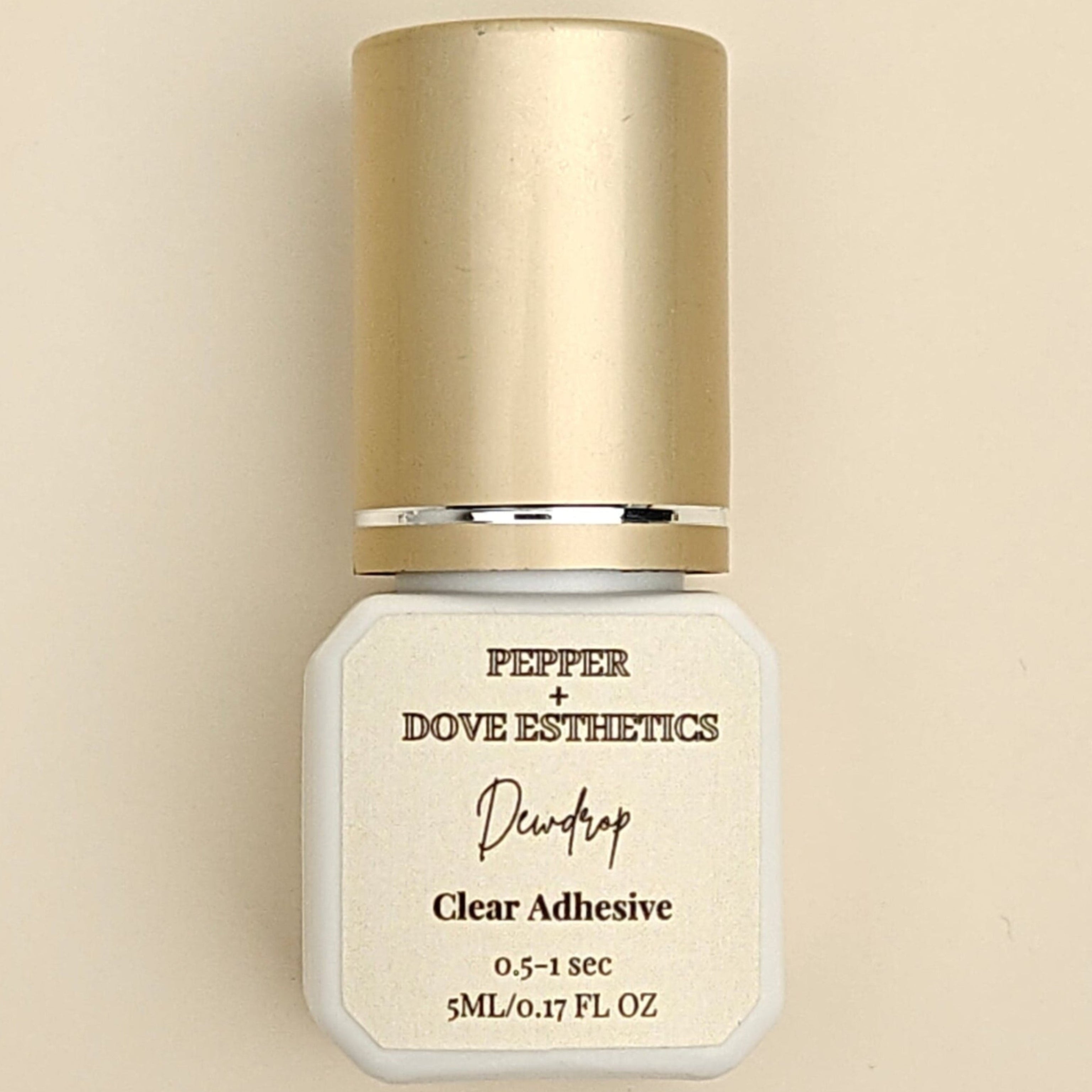 A bottle of Pepper + Dove Esthetics Nailtop Clear Adhesive centered on a warm beige background.